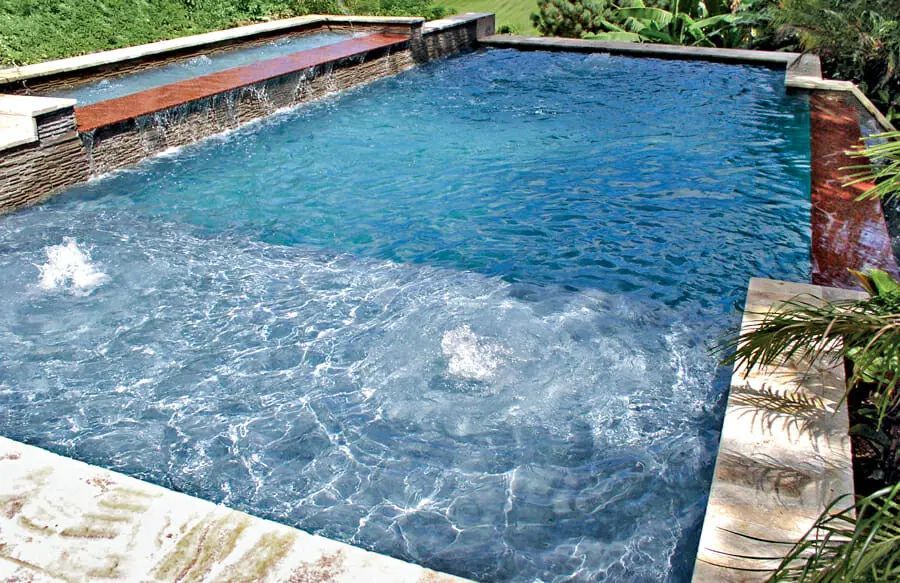 Blue swimming pool with rippling water, stone edge, and surrounding greenery