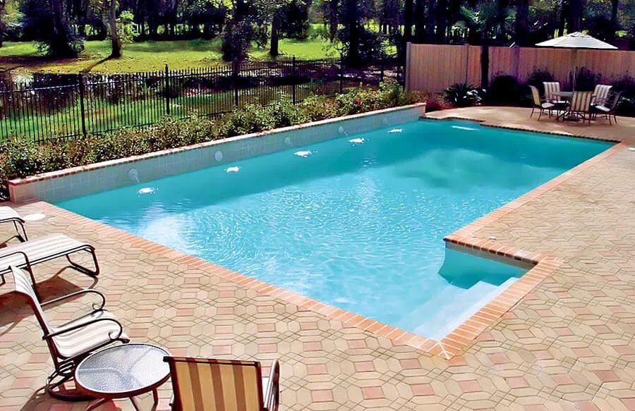 Backyard swimming pool with turquoise water, brick patio, lounge chairs, and a grassy yard