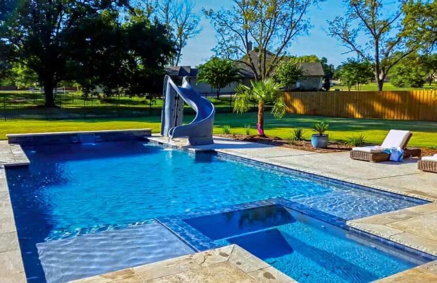 Backyard swimming pool with a blue water slide, spa, and lounge chairs on a sunny day