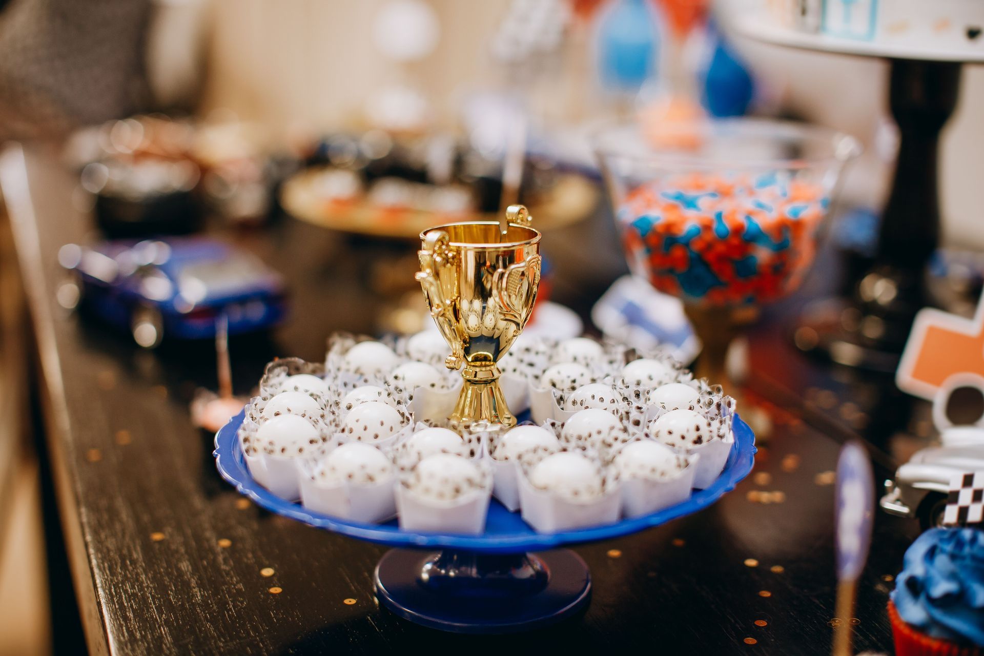 Doces confeitados brancos e azuis dispostos sobre uma mesa, com um troféu dourado como peça central.
