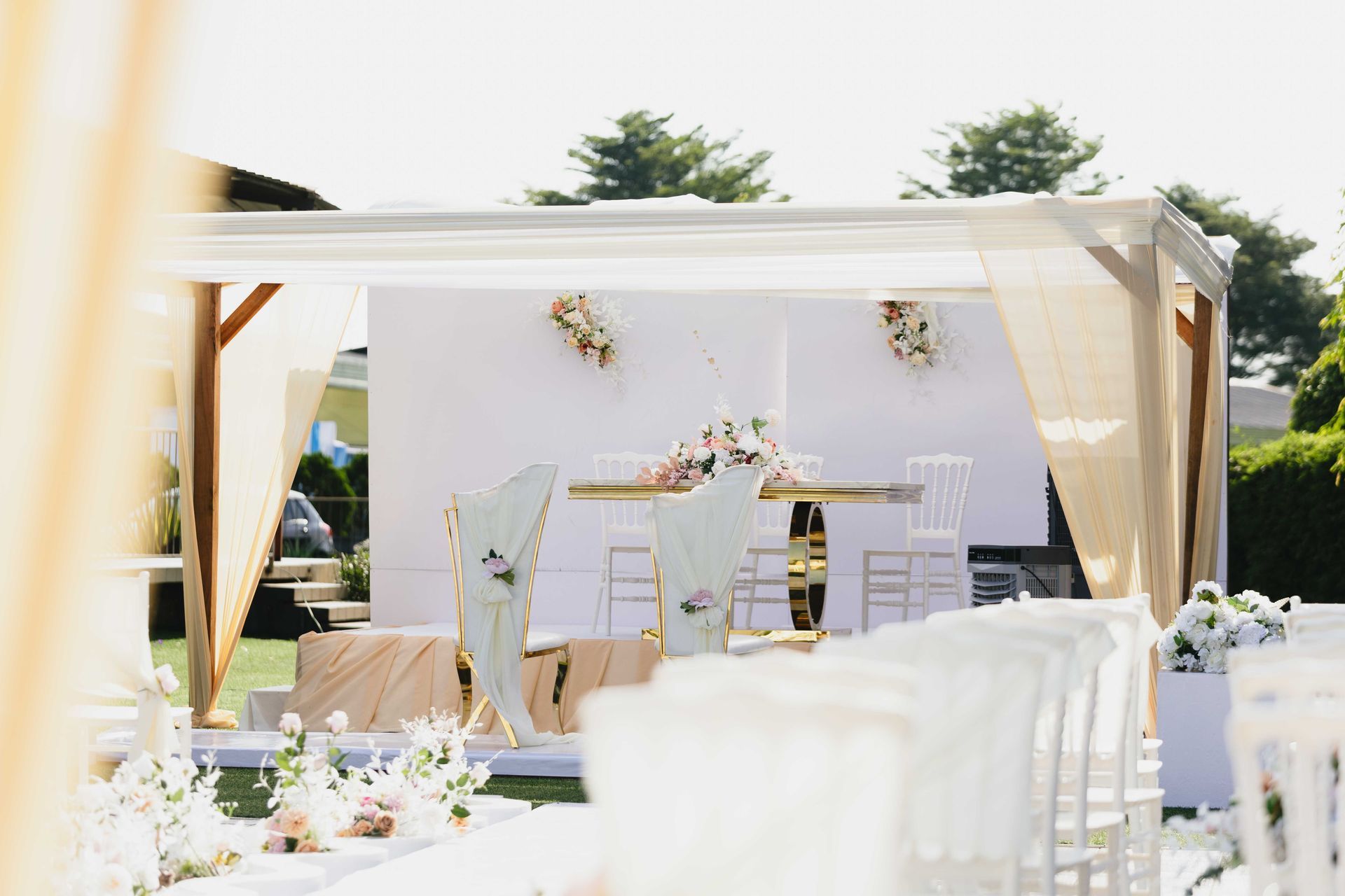 Recepção de casamento ao ar livre sob um dossel branco com cadeiras brancas e decoração floral.