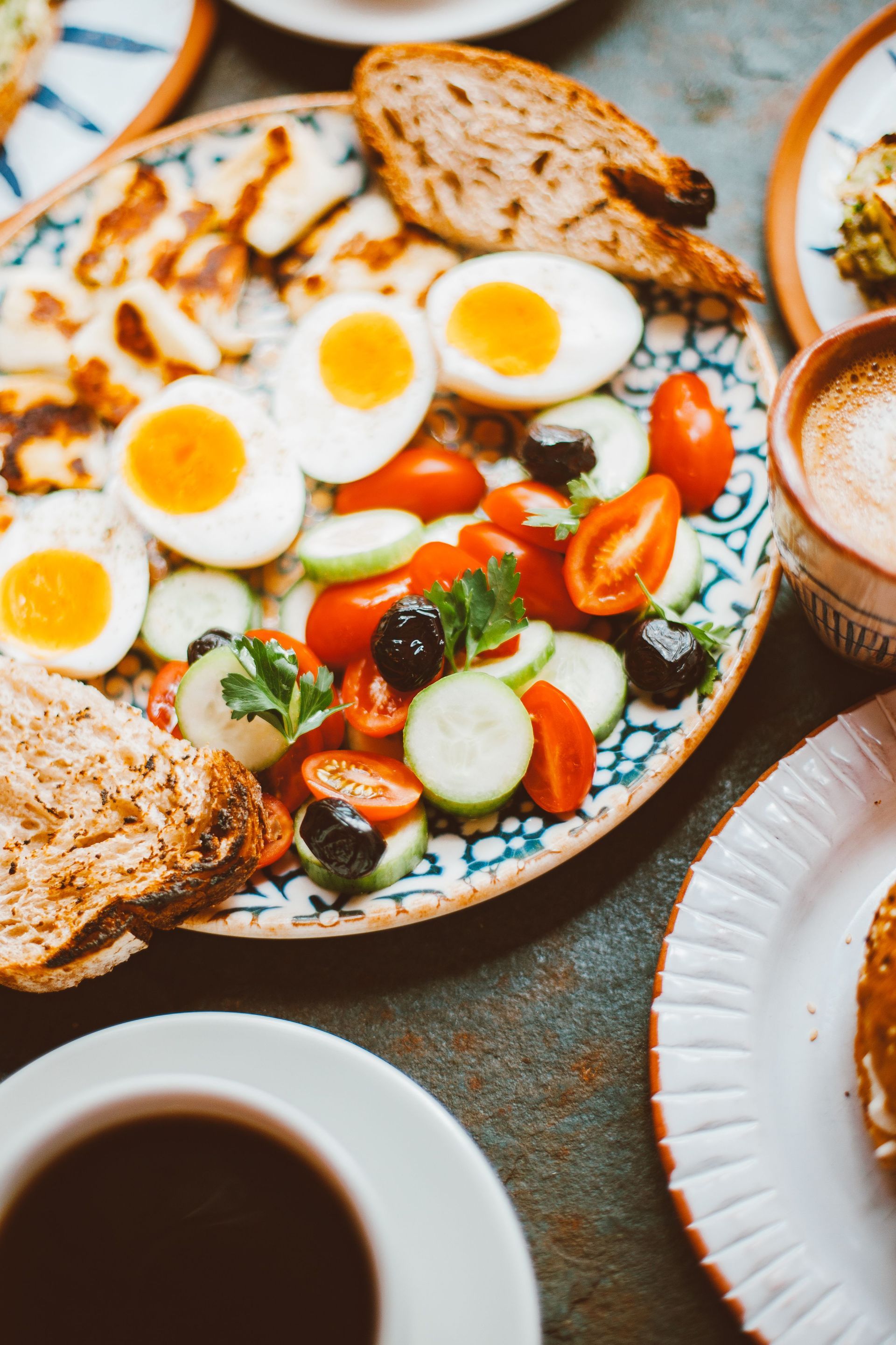 Prato de brunch com ovos cozidos fatiados, torradas, legumes e café sobre uma mesa.