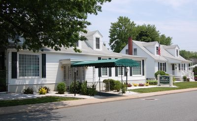 A street-level view of a white, multi-story building with a green awning, adjacent to a similar house on a sunny day.