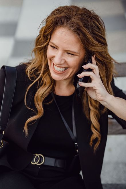 Smiling woman in a black outfit talking on a phone while sitting on steps