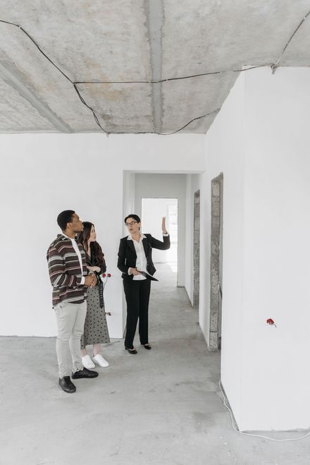 Three people inspecting an unfinished hallway in a bare, white interior space.