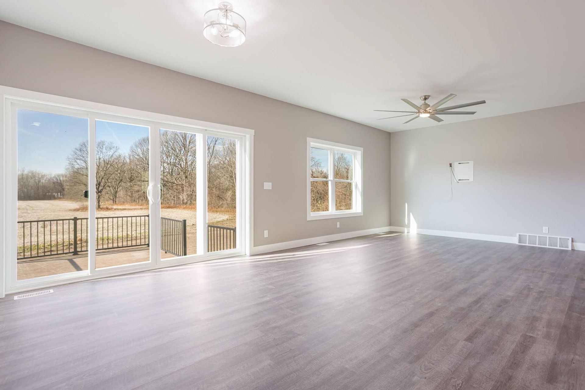 Spacious empty living room with gray floors, large sliding glass doors, and ceiling fan.