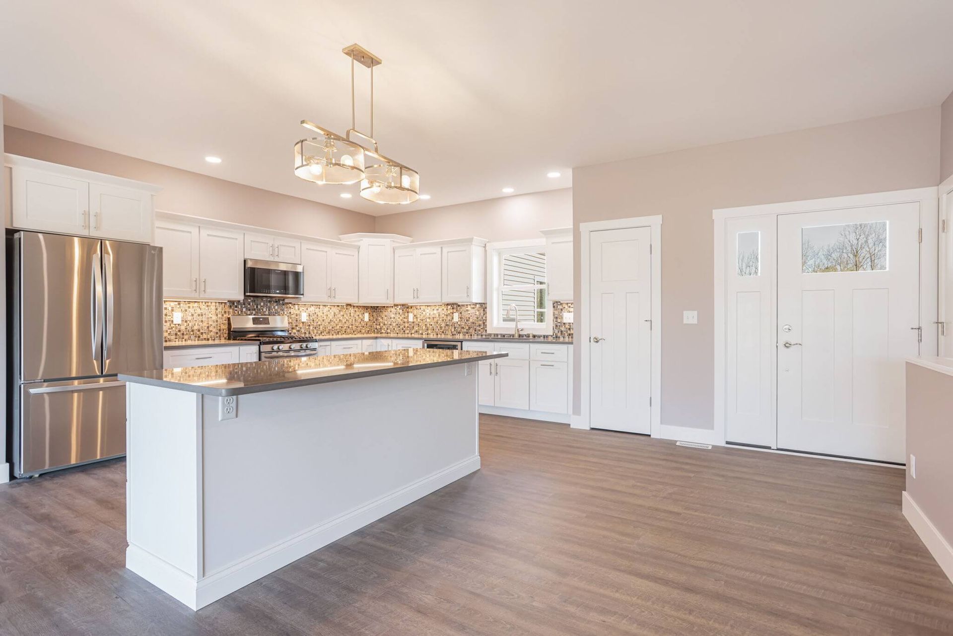 Bright open kitchen with white cabinets, stainless steel fridge, large island, and wood-look flooring
