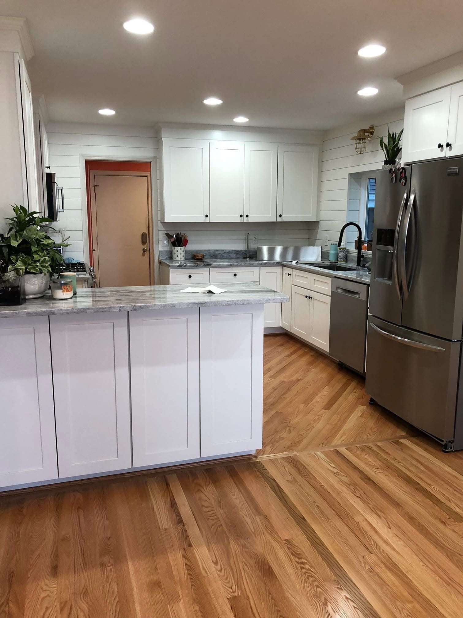 Bright modern kitchen with white cabinets, stainless steel fridge, island, and wood floors