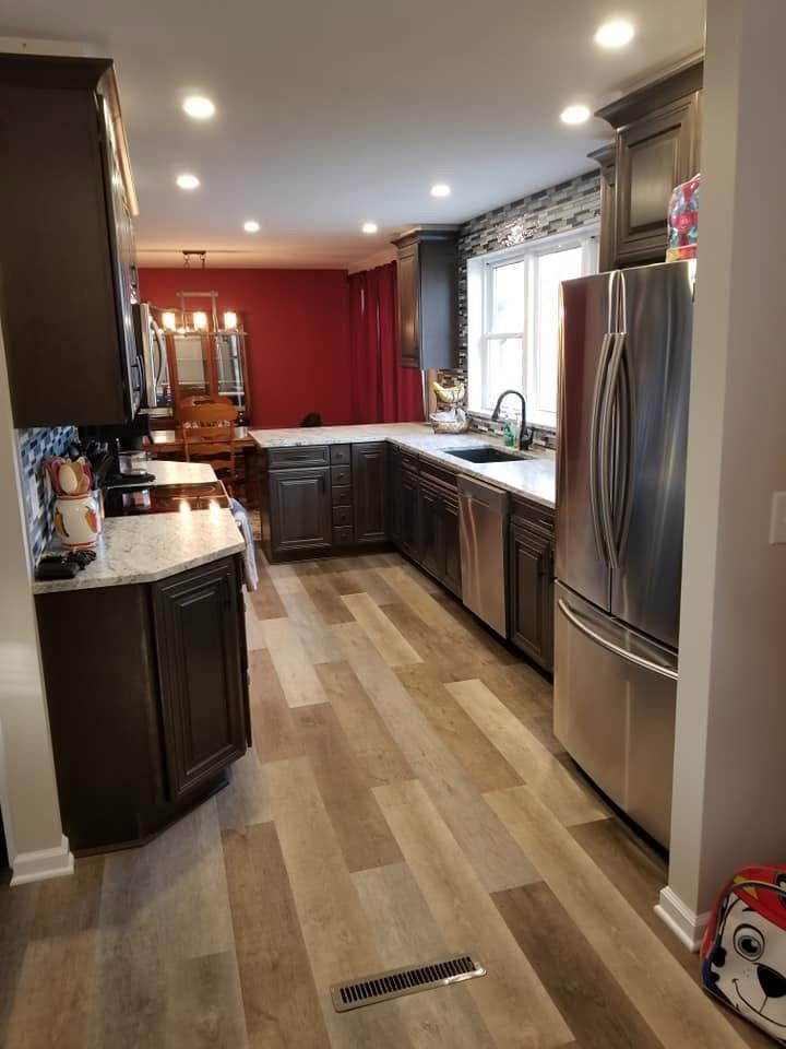 Bright kitchen with dark wood cabinets, stainless steel refrigerator, and light wood floor.