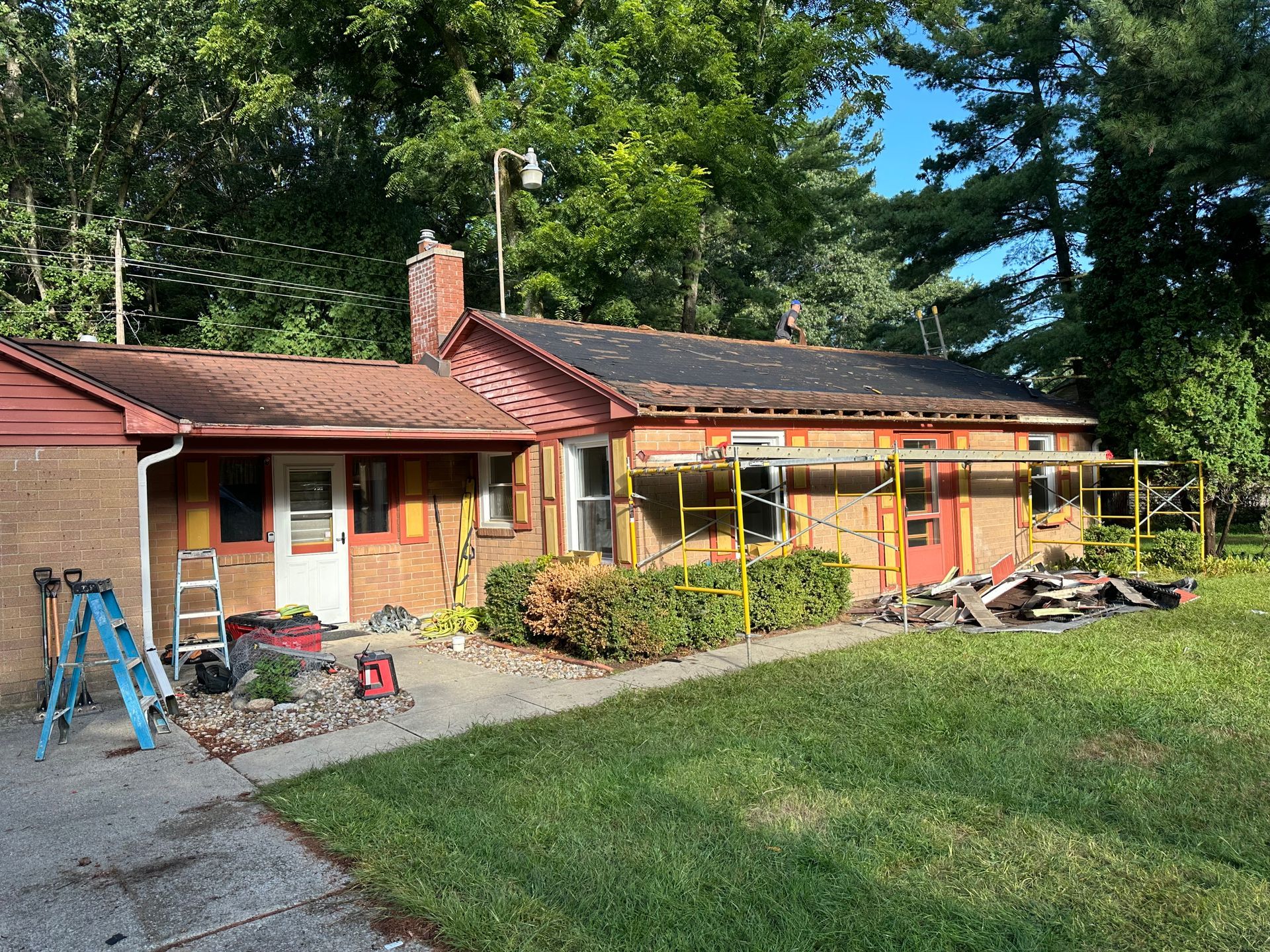 House exterior under renovation with scaffolding, tools, and a grassy front yard