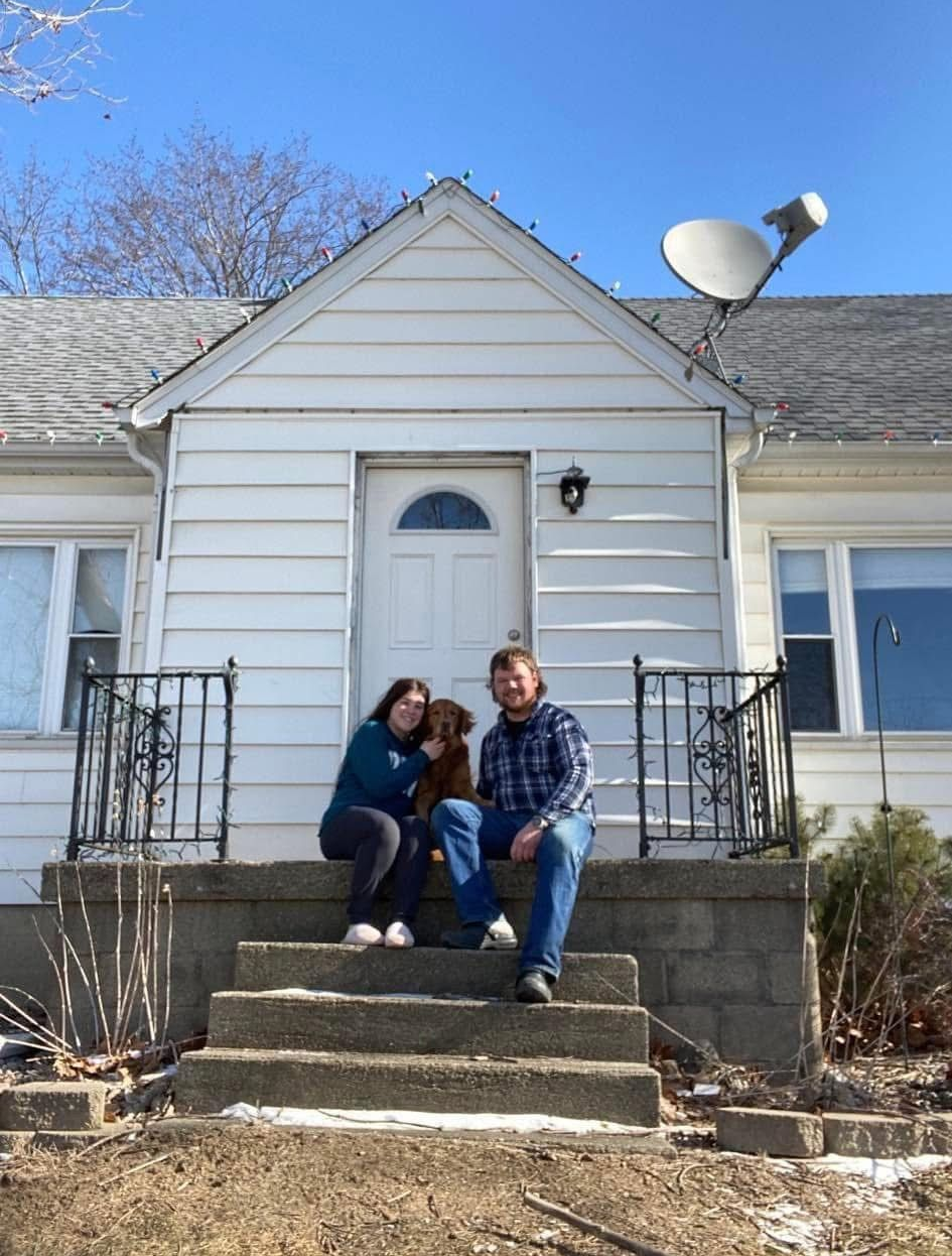 Two people sitting on front steps of a white house on a sunny day