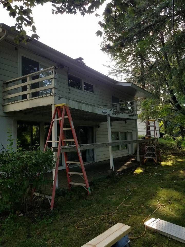 Two-story house with a red ladder leaning against the porch in a leafy yard