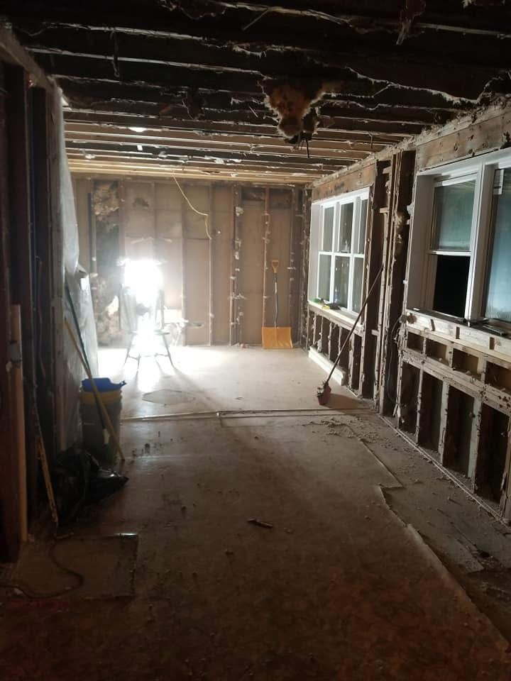 Interior of a stripped room under renovation, with exposed studs, unfinished walls, and bright light at the far end.