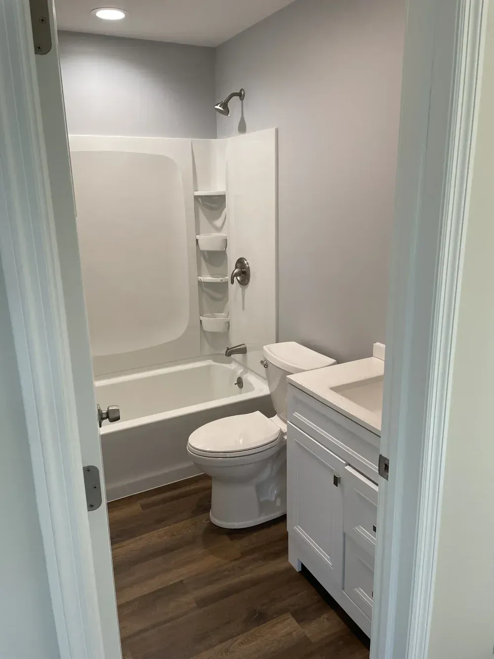 Small bathroom with a white tub, toilet, and vanity, viewed through the doorway.