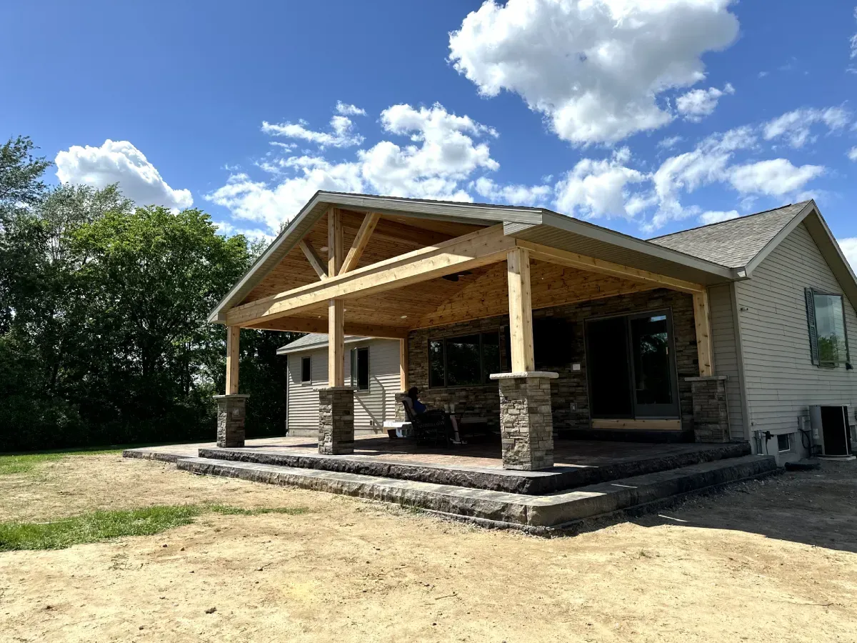 Covered porch with stone pillars on a house under a blue sky with clouds