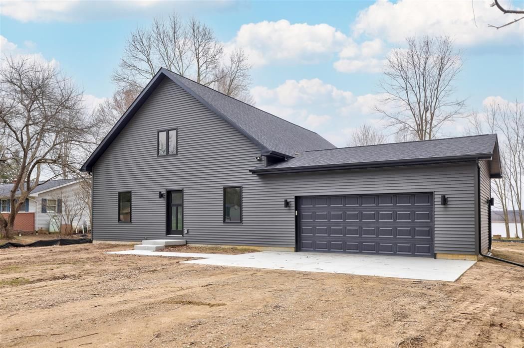 Gray modern house with black roof and garage, viewed from the front under a partly cloudy sky