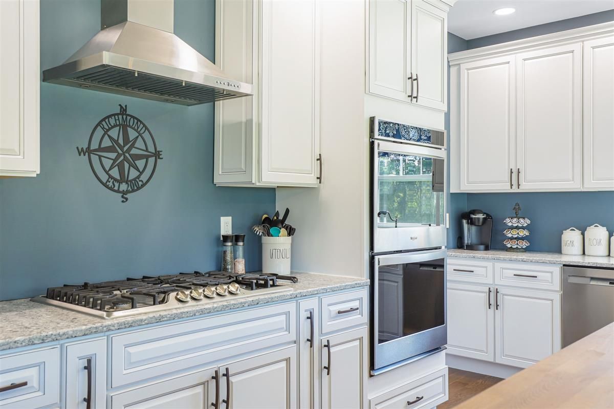 Bright white kitchen with blue backsplash, gas stove, stainless vent hood, and built-in oven.