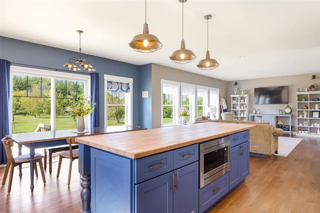 Bright modern kitchen and dining area with blue island, wood floors, pendant lights, and patio view
