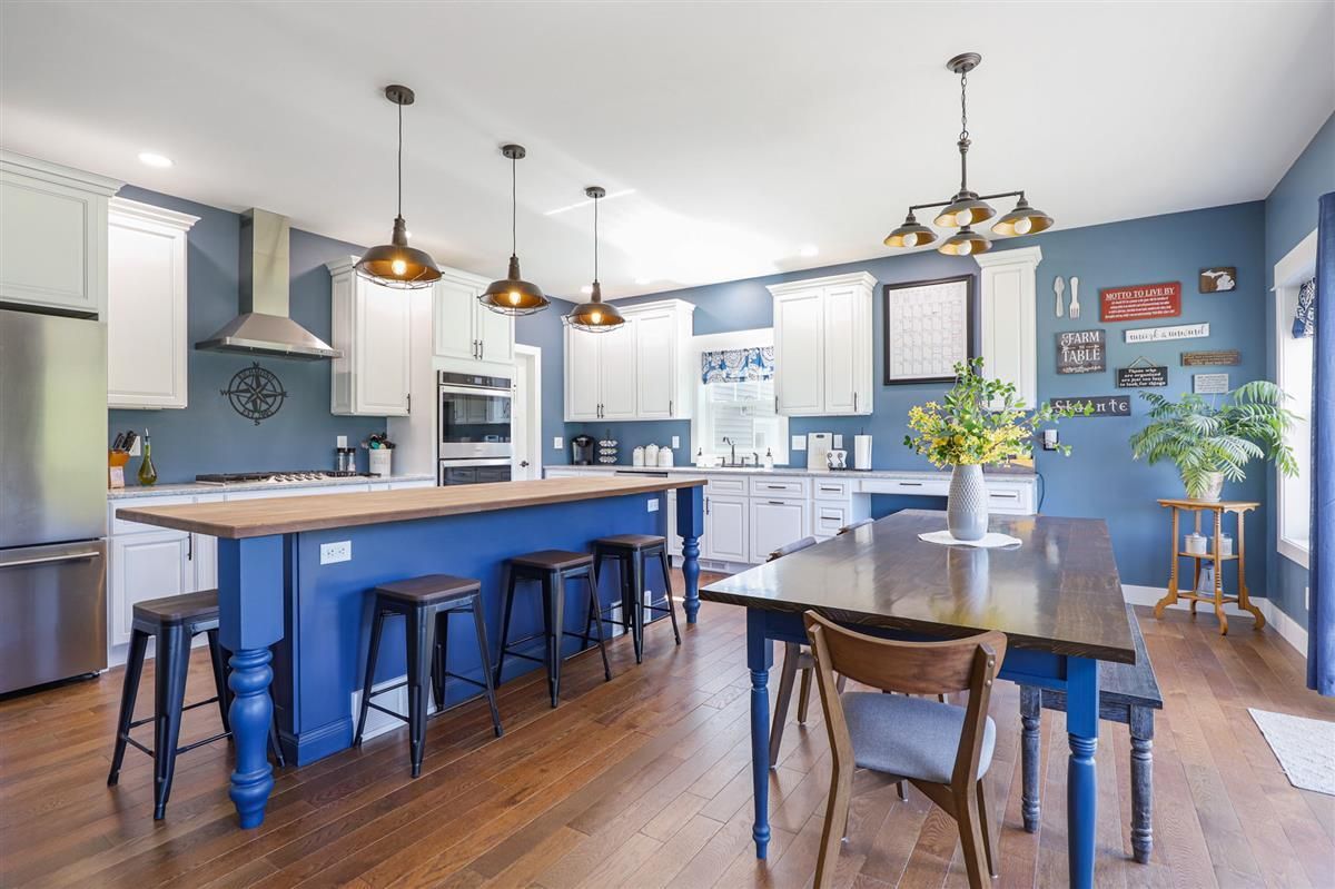 Bright modern kitchen with blue island, wooden floors, pendant lights, and dining table by large windows