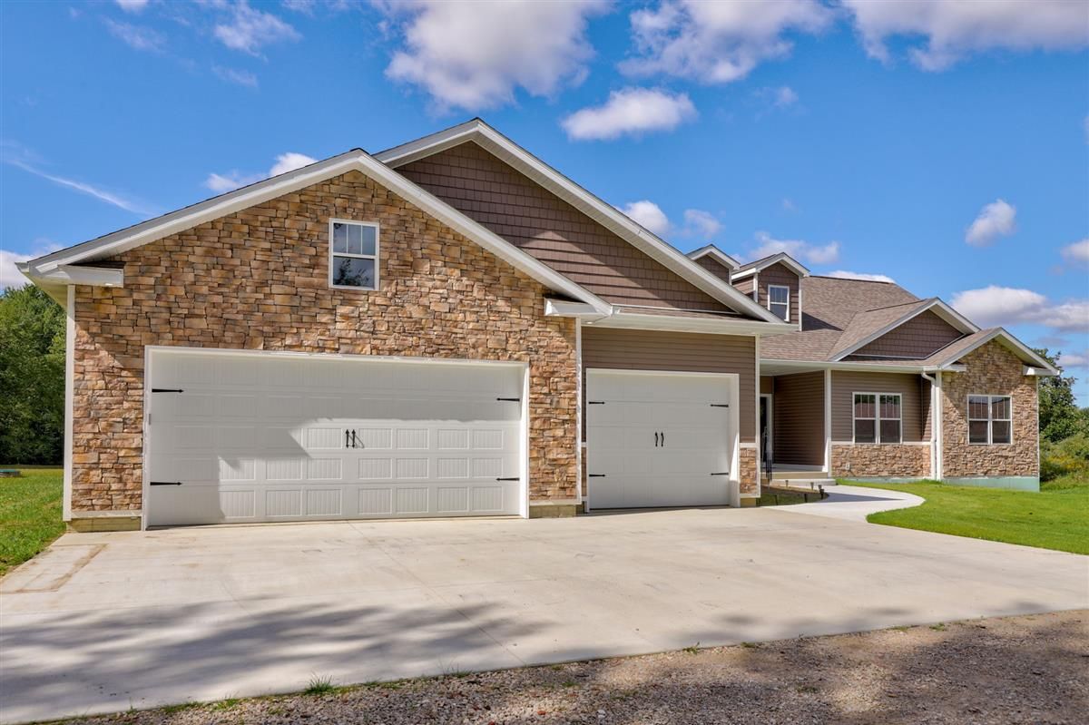 Brick suburban house with white garage doors and a front porch under a blue sky