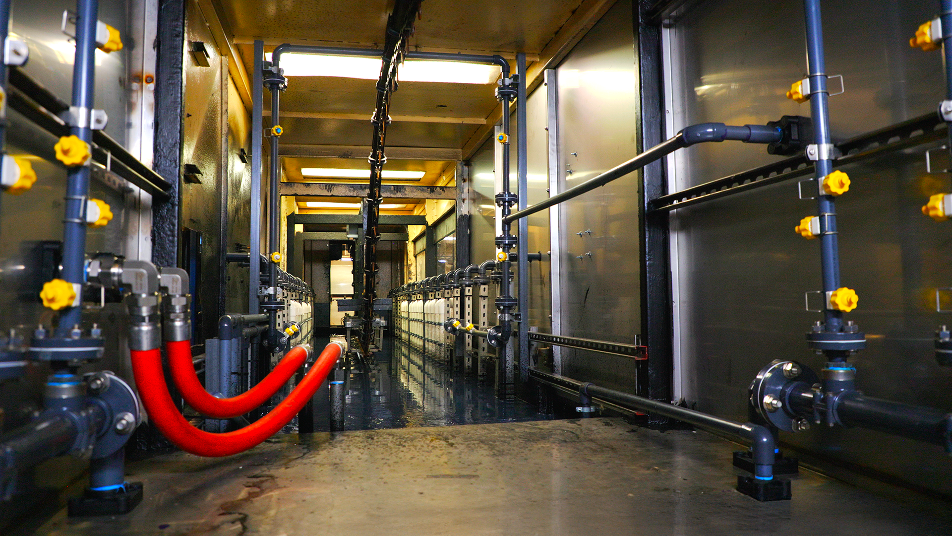 Industrial corridor with black pipes and bright red hoses in a metallic, dimly lit facility