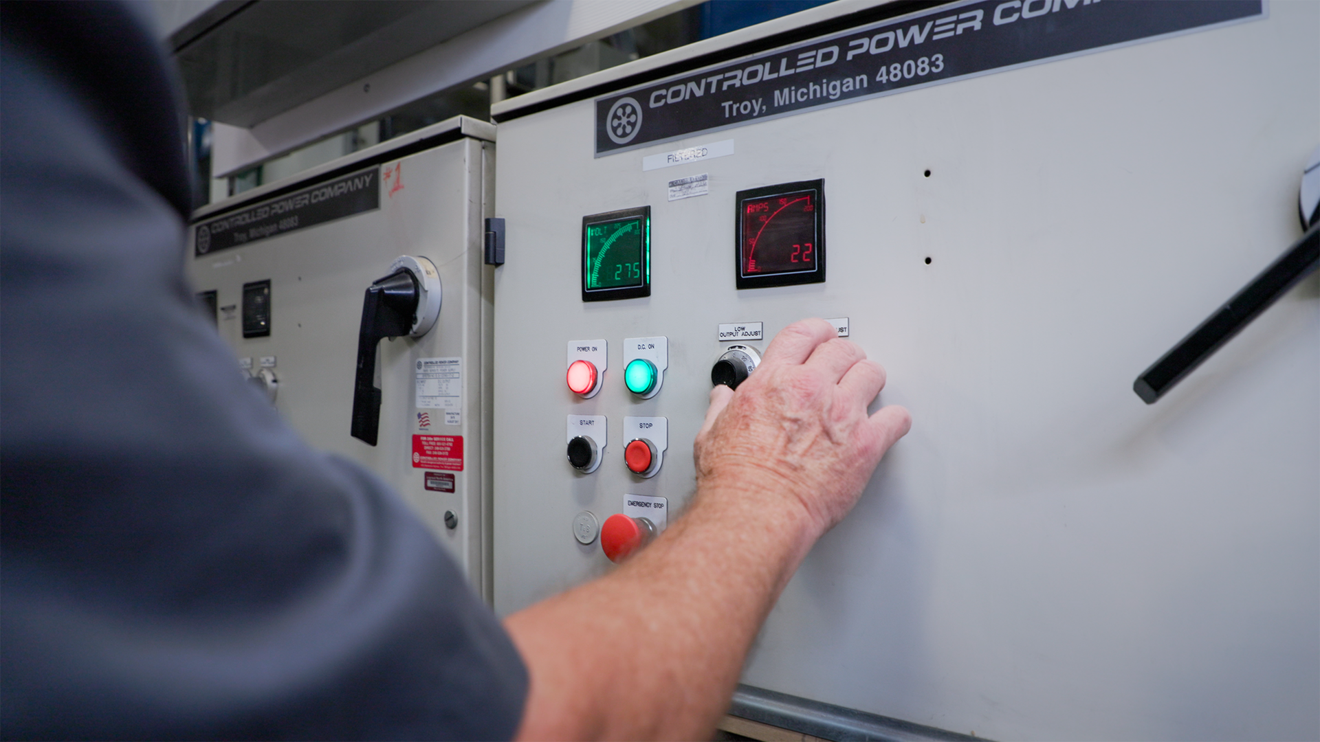 Person adjusts controls on a panel with lit green and red buttons in an industrial setting