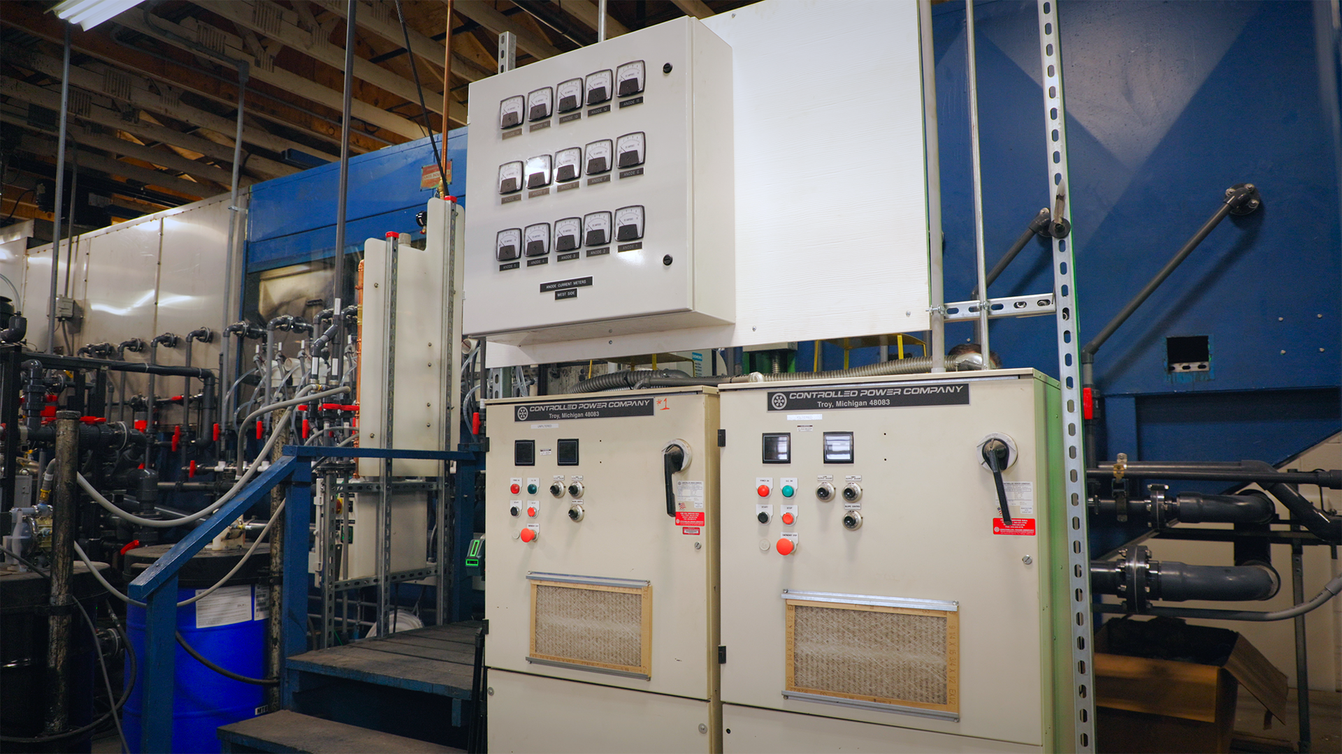 Industrial electrical control panels and equipment in a factory setting with blue machinery and metal framework