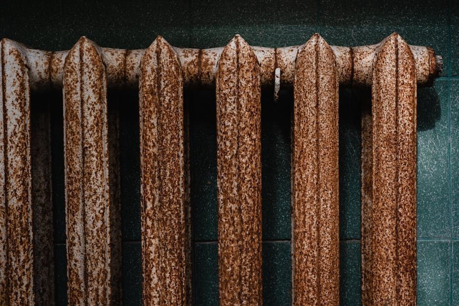 Rusty vertical radiator pipes against a dark green tiled wall