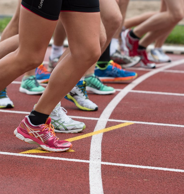 A group of people on a track, preparing to run, wearing tennis shoes and getting ready for their race or workout.