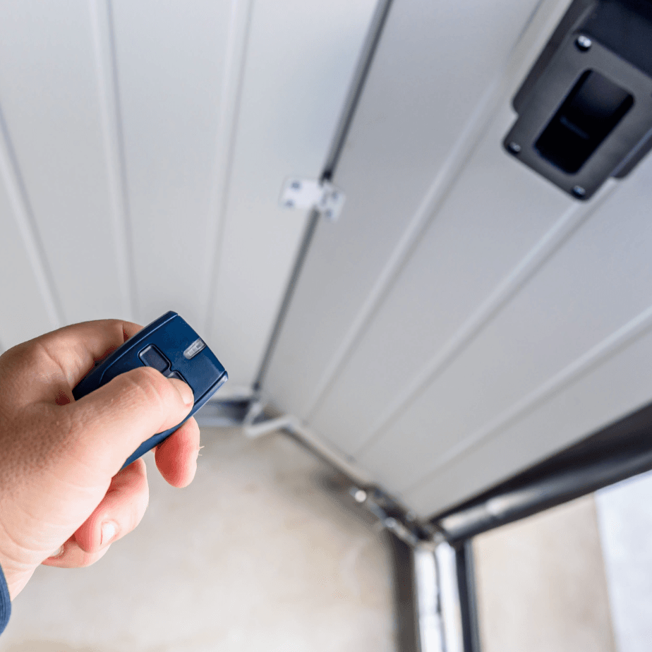 Hand holding a blue garage door remote near a white garage door opener panel