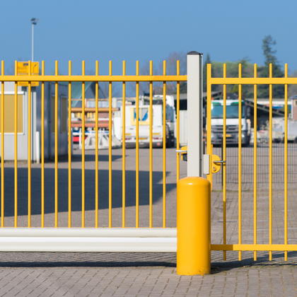 Yellow metal security gate across an entrance, with parked vehicles and buildings in the background.