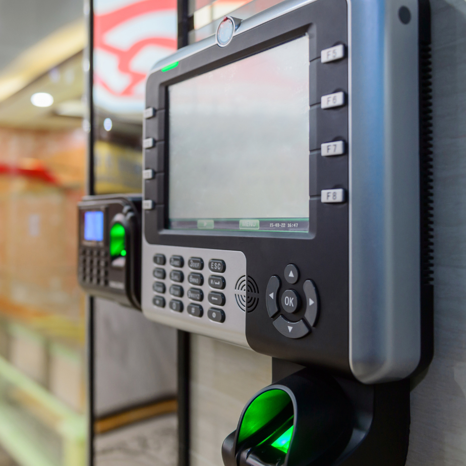 Wall-mounted time clock with keypad and green-lit fingerprint scanner in an office hallway