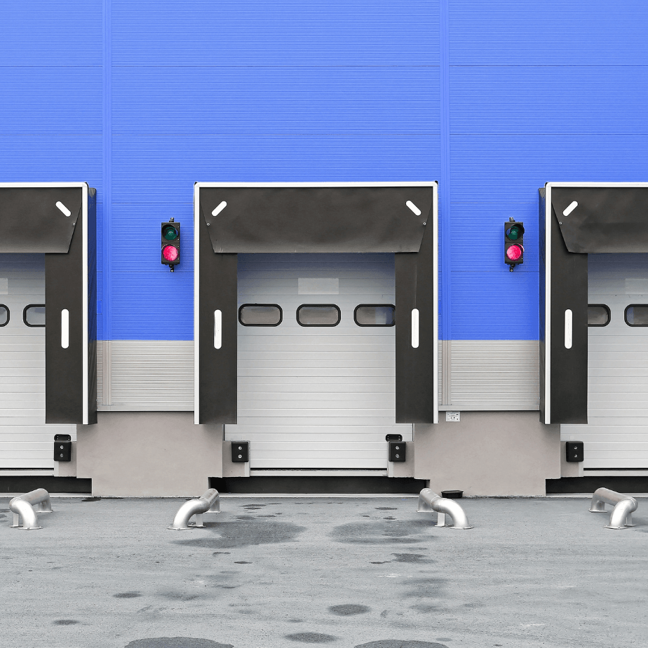 Three loading docks with gray doors on a blue industrial wall, birds on the pavement below.