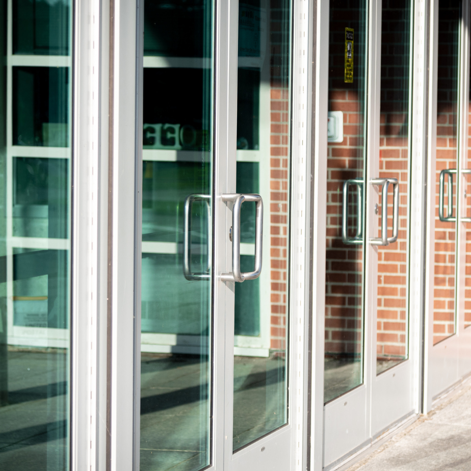 Glass storefront doors with metal handles beside a brick wall and sidewalk