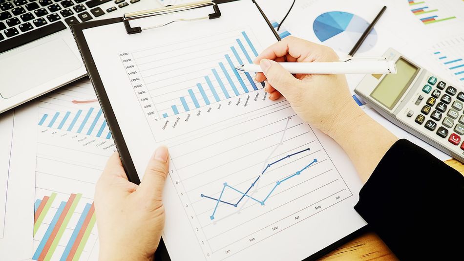 Hands reviewing financial charts and graphs on a desk with a calculator and pen.