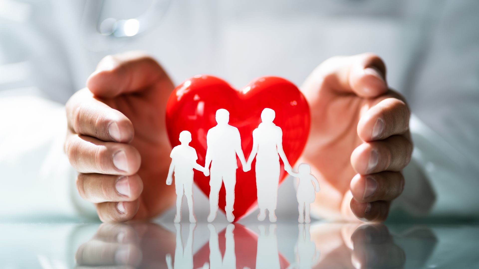 Hands protecting a red heart with a family silhouette inside, symbolizing healthcare or family protection