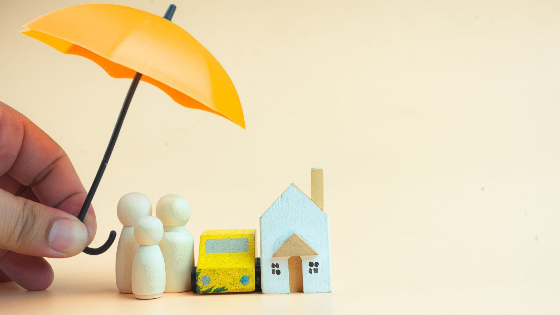 Miniature people under a yellow umbrella beside toy houses and a small bus on a light background