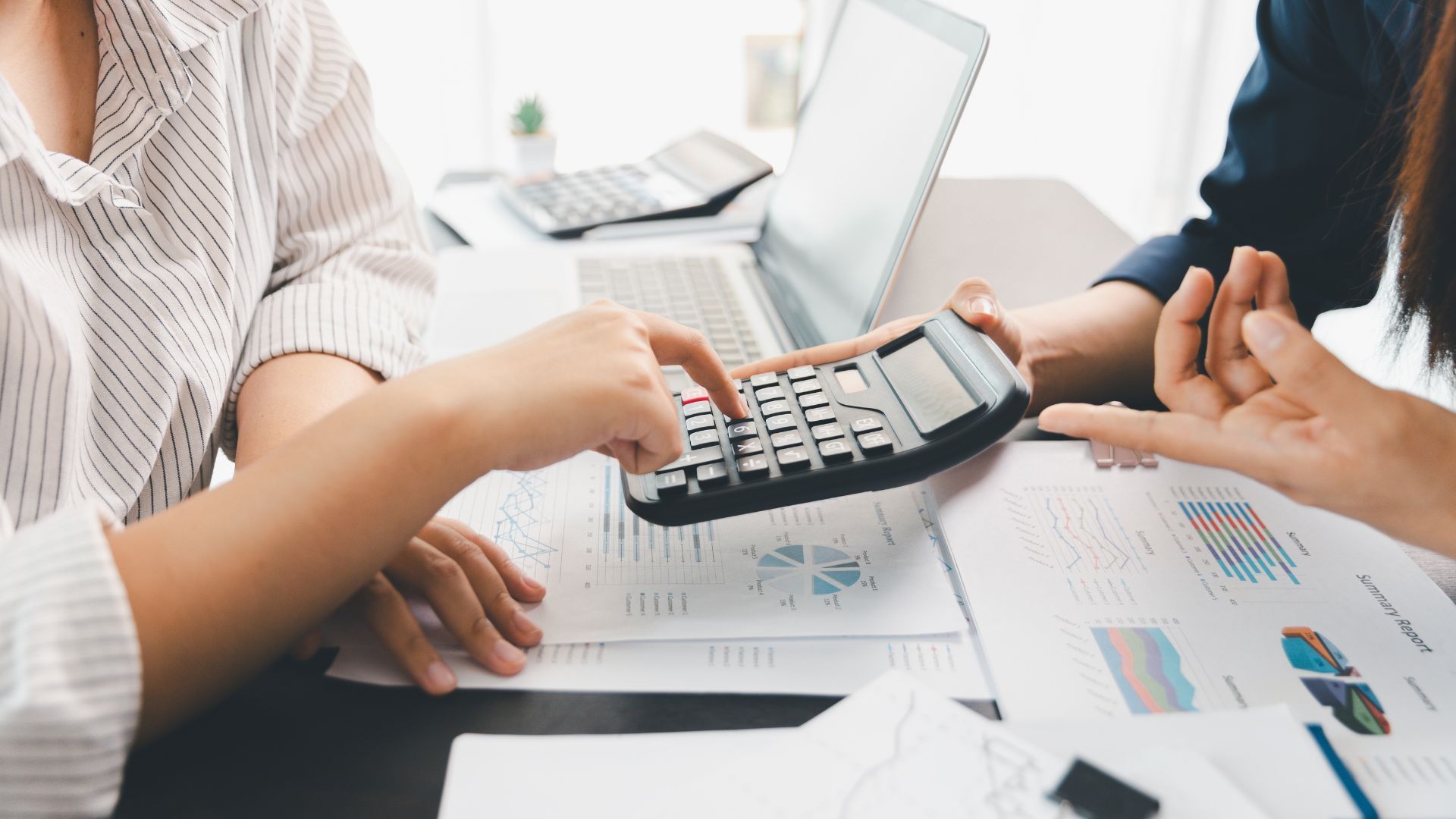 Two people use a calculator over financial charts during a meeting