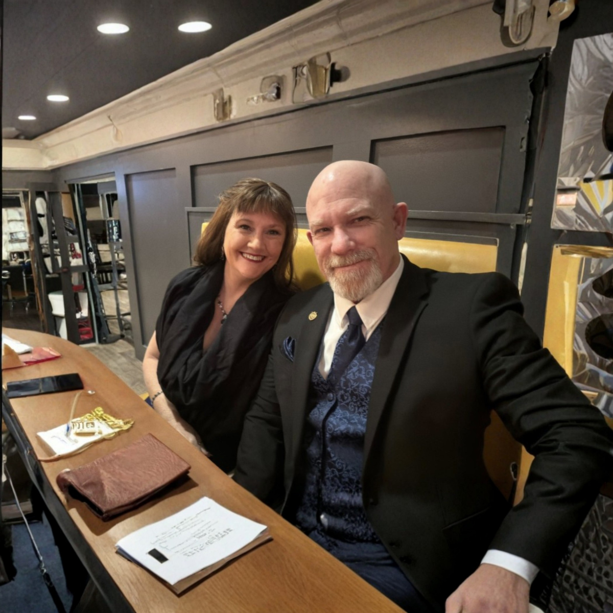 Two smiling people in formal attire seated at a table in a warmly lit interior.