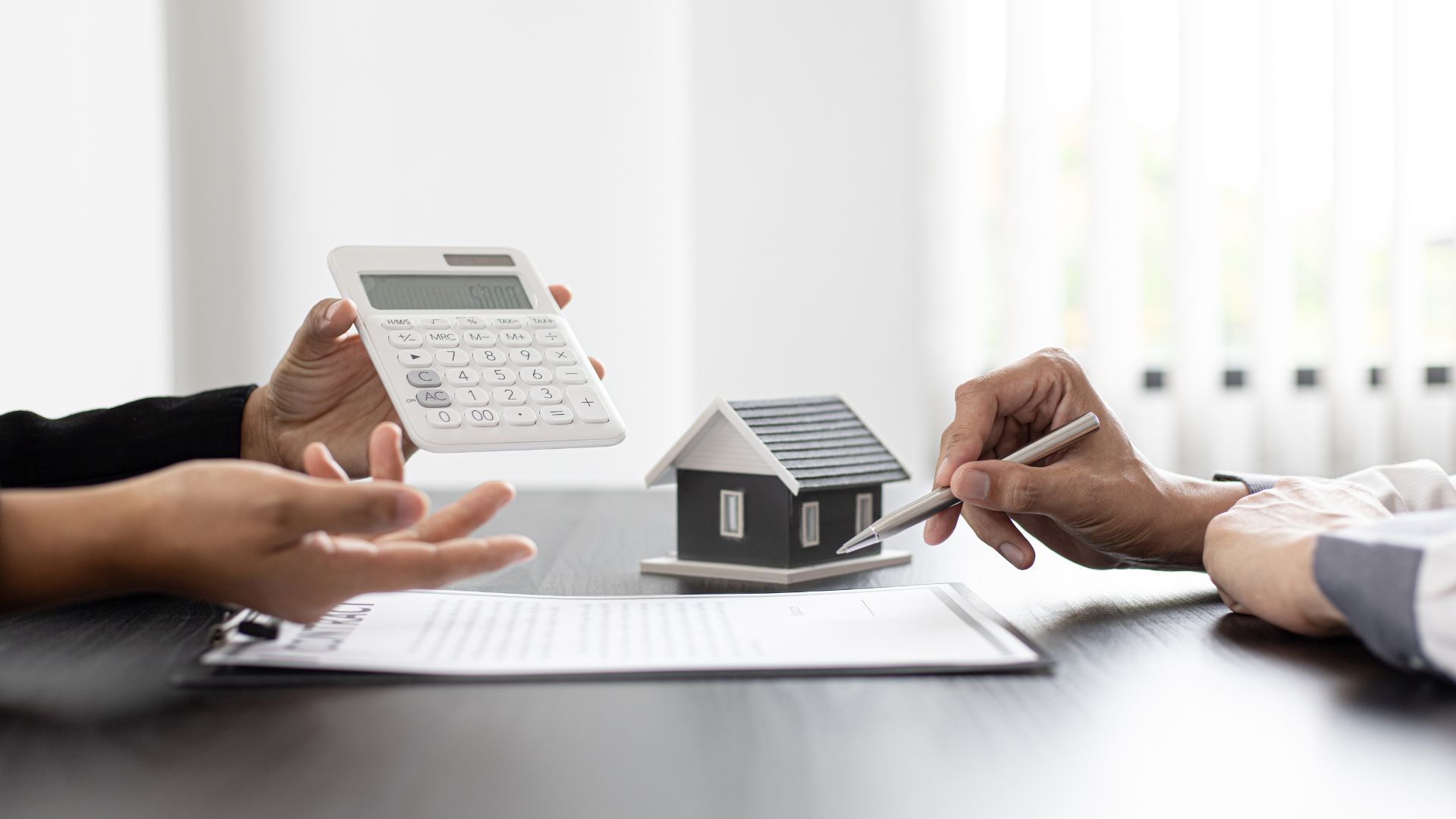 Hands reviewing a house model and calculator during a real estate meeting