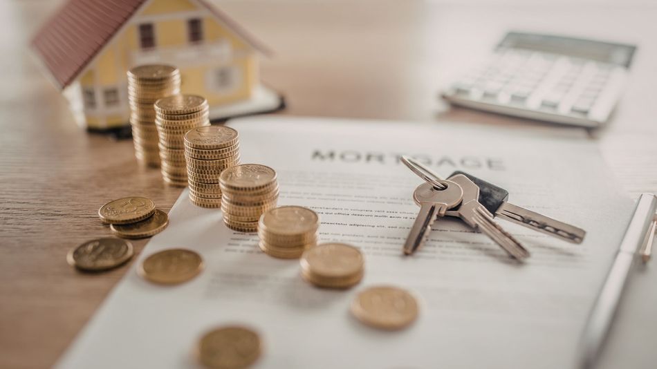 Coins, house key, and small house model on a mortgage document with calculator in the background
