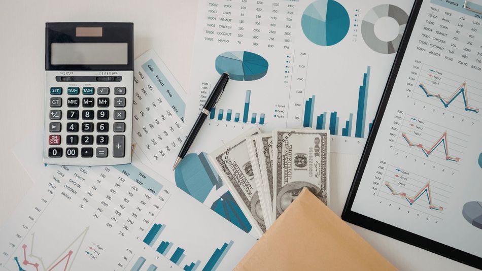 Calculator, eyeglasses, money, and charts on a desk, suggesting financial analysis and budgeting.