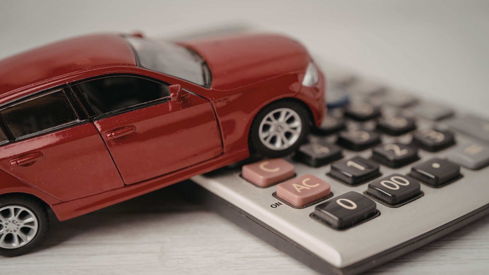 Red toy car resting on a calculator, symbolizing car expenses or insurance costs