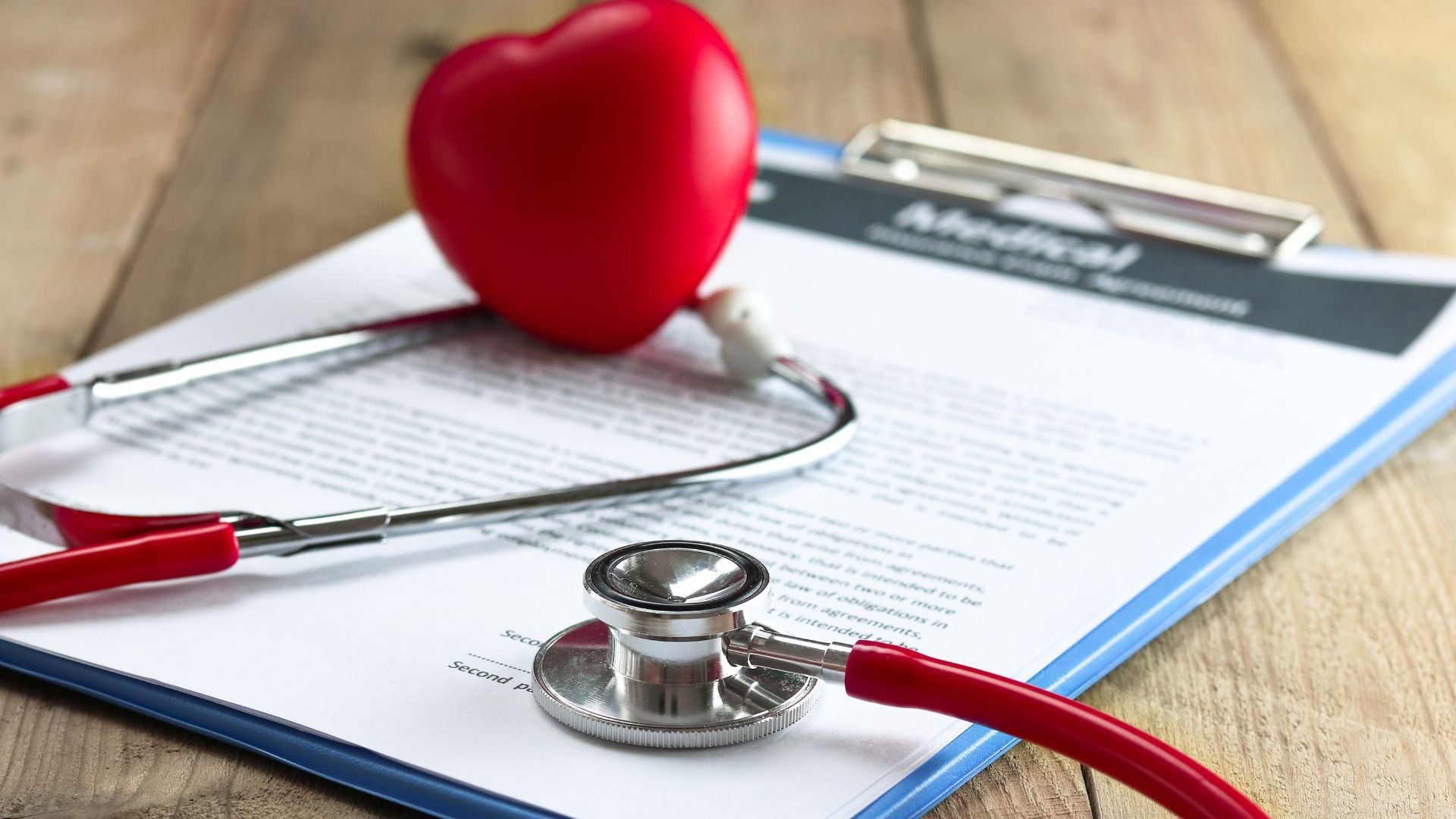 Stethoscope and red heart on a clipboard with medical paperwork on a desk