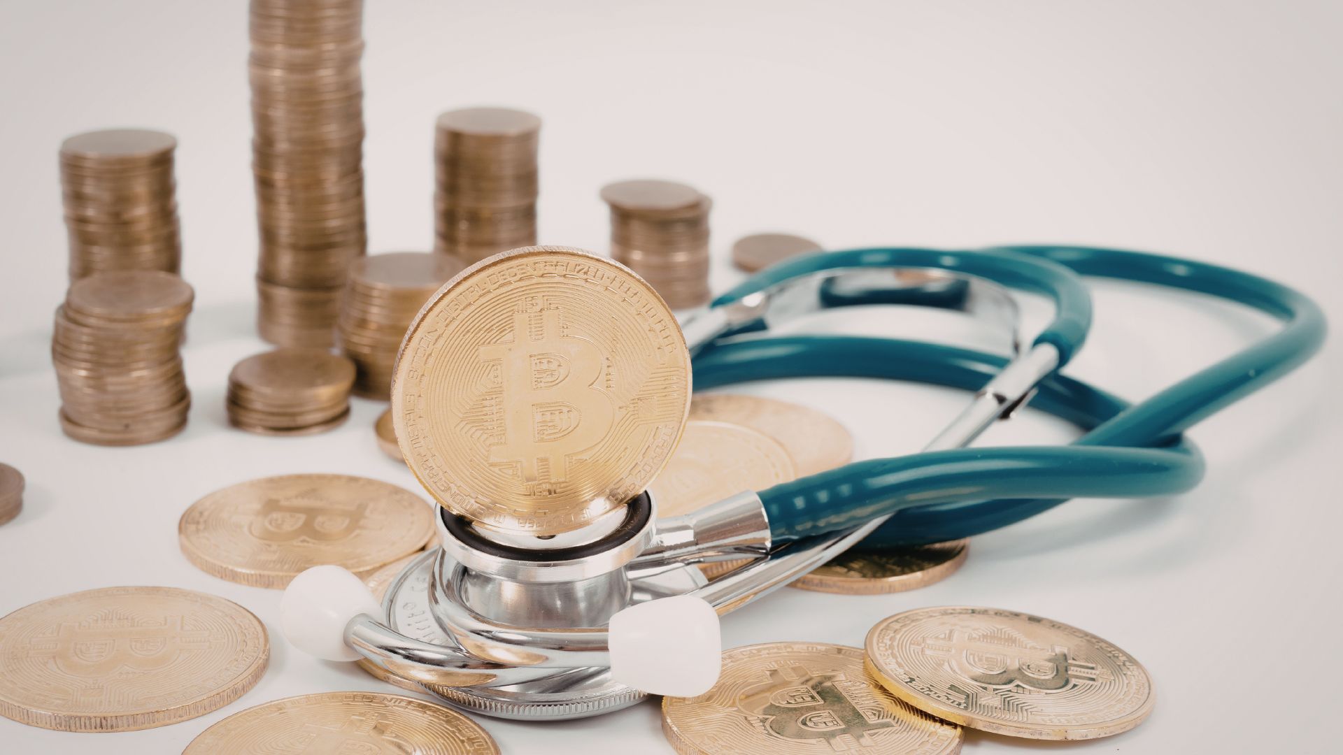 Stethoscope beside stacked coins and a coin under a magnifying glass, symbolizing healthcare costs
