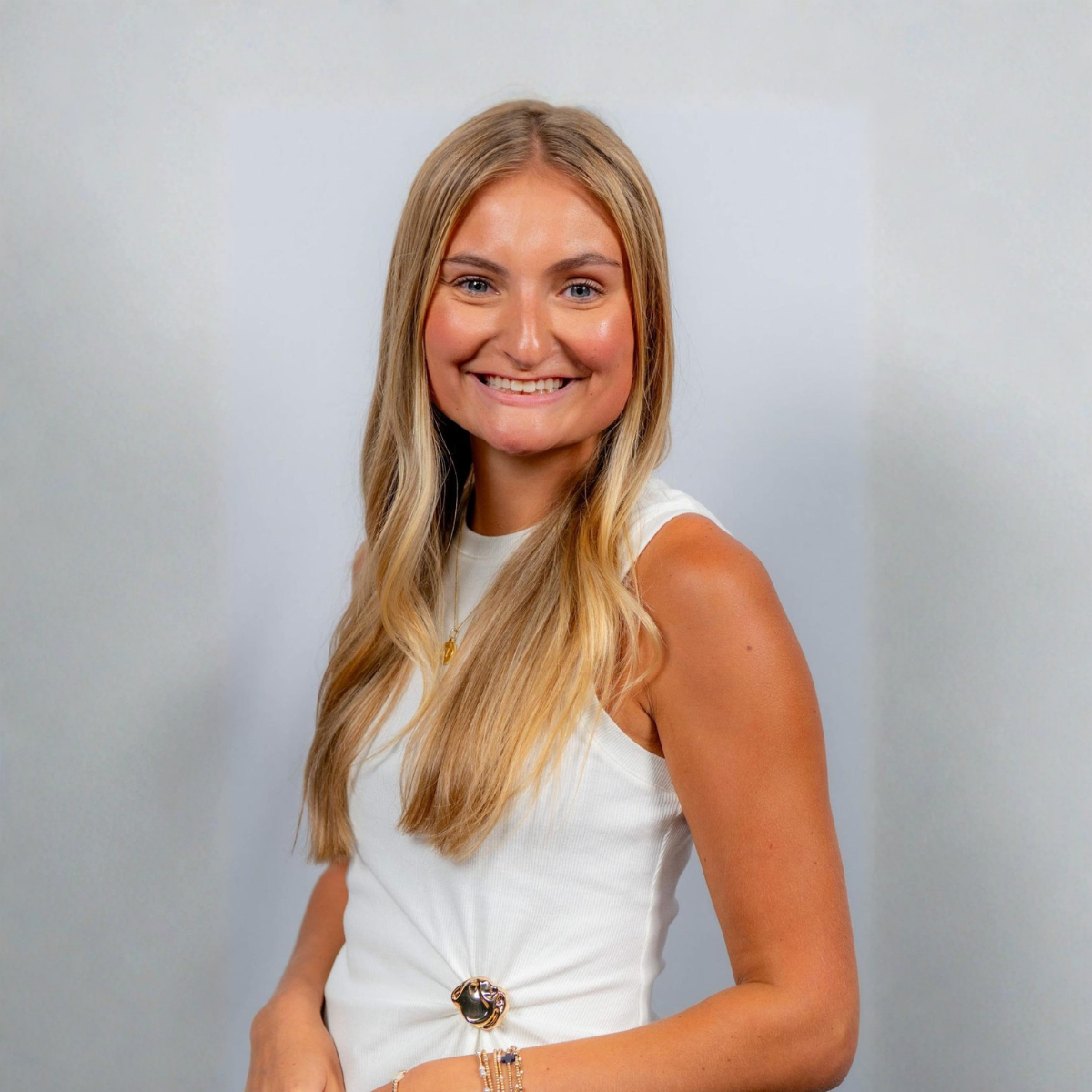 Smiling woman in a white sleeveless dress against a light gray background.