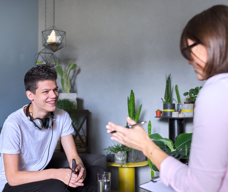Teenager smiling during counseling session with a woman. Room with plants.
