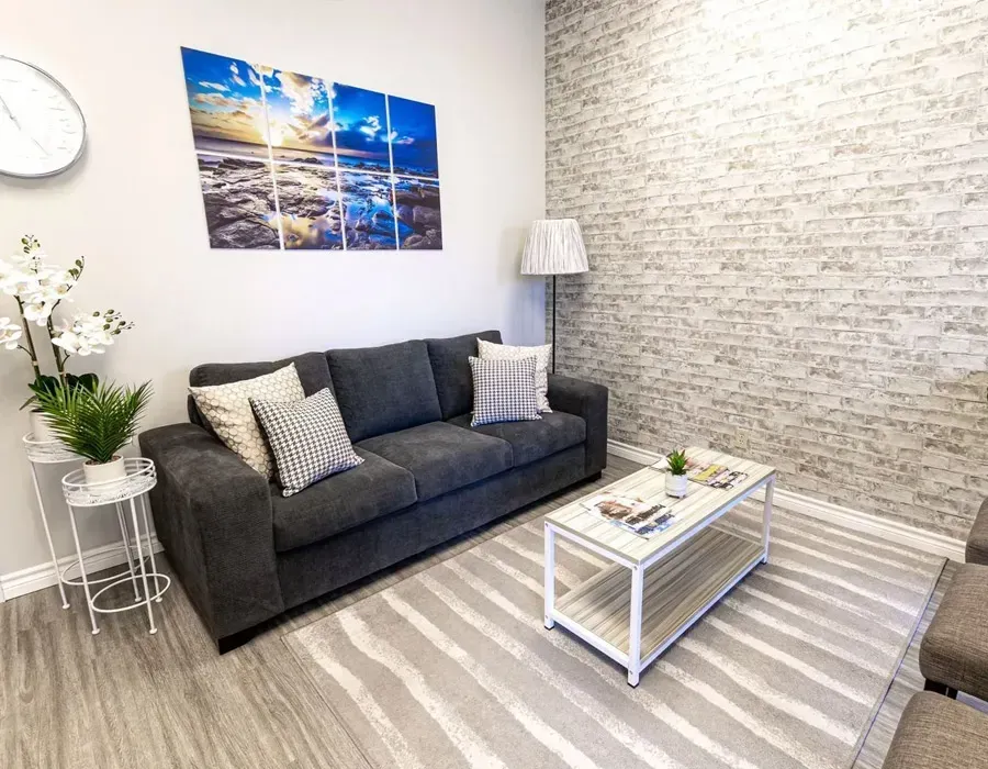 Waiting room with gray sofa, brick accent wall, and ocean-themed art.
