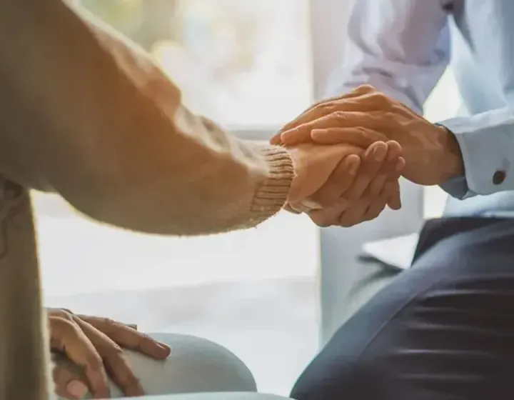 Person comforting another, holding their hands in a supportive gesture.
