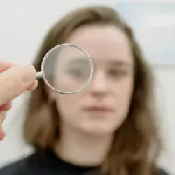 Hand holding a small magnifying lens in front of a blurred face